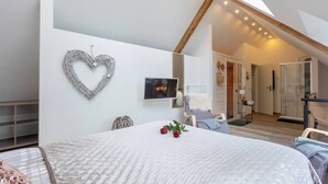 A bedroom with a large bed, a heart-shaped decoration, a TV displaying 'NETFLIX', and a staircase leading to another room. - Holiday Apartment "Kleine Auszeit" – Your Place to Relax (Mürlenbach)