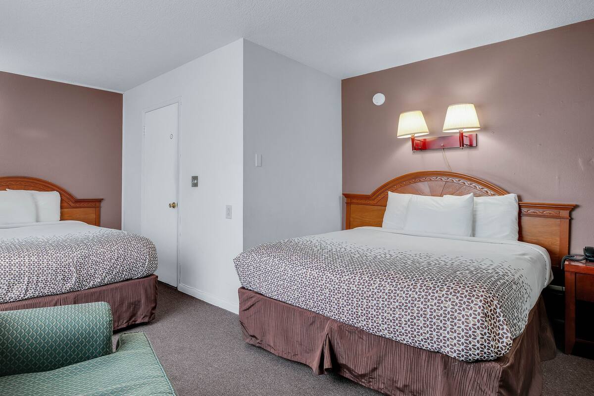 Et hotelværelse med to senge, en stol, et natbord og vægmonterede lamper.