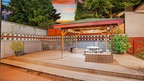 Un área de patio techada con piso de madera, una mesa y sillas, y plantas en macetas.