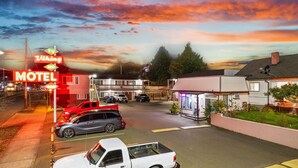 Un motel con un letrero de neón, un estacionamiento con varios autos y un edificio con balcón.