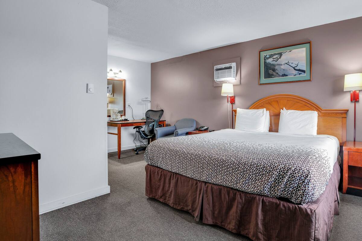 Et hotelværelse med en seng, et skrivebord med stol, et spejl, en lampe og et billede på væggen.