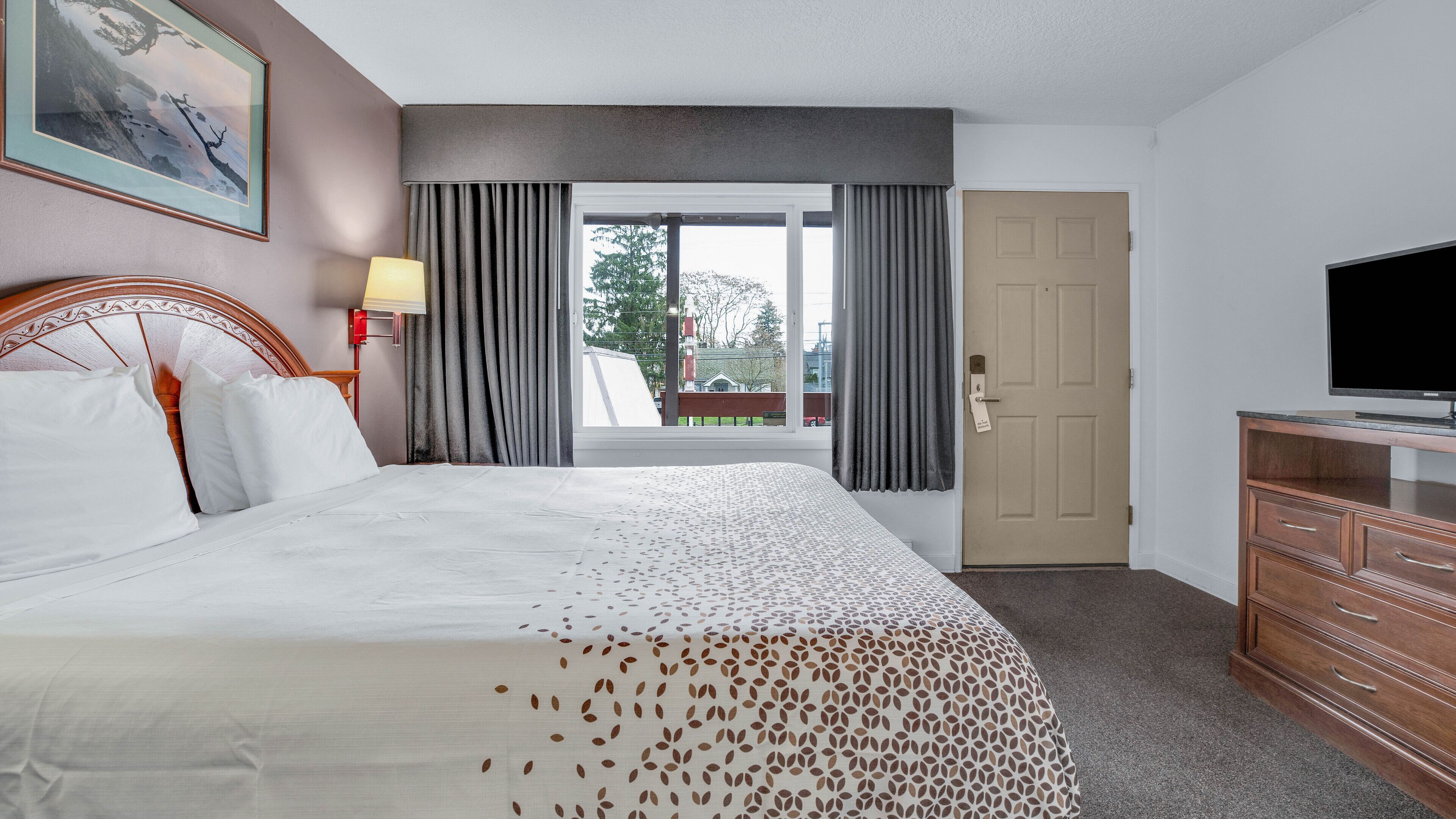 Une chambre d’hôtel avec un lit, une télévision, une commode et une fenêtre avec des rideaux.