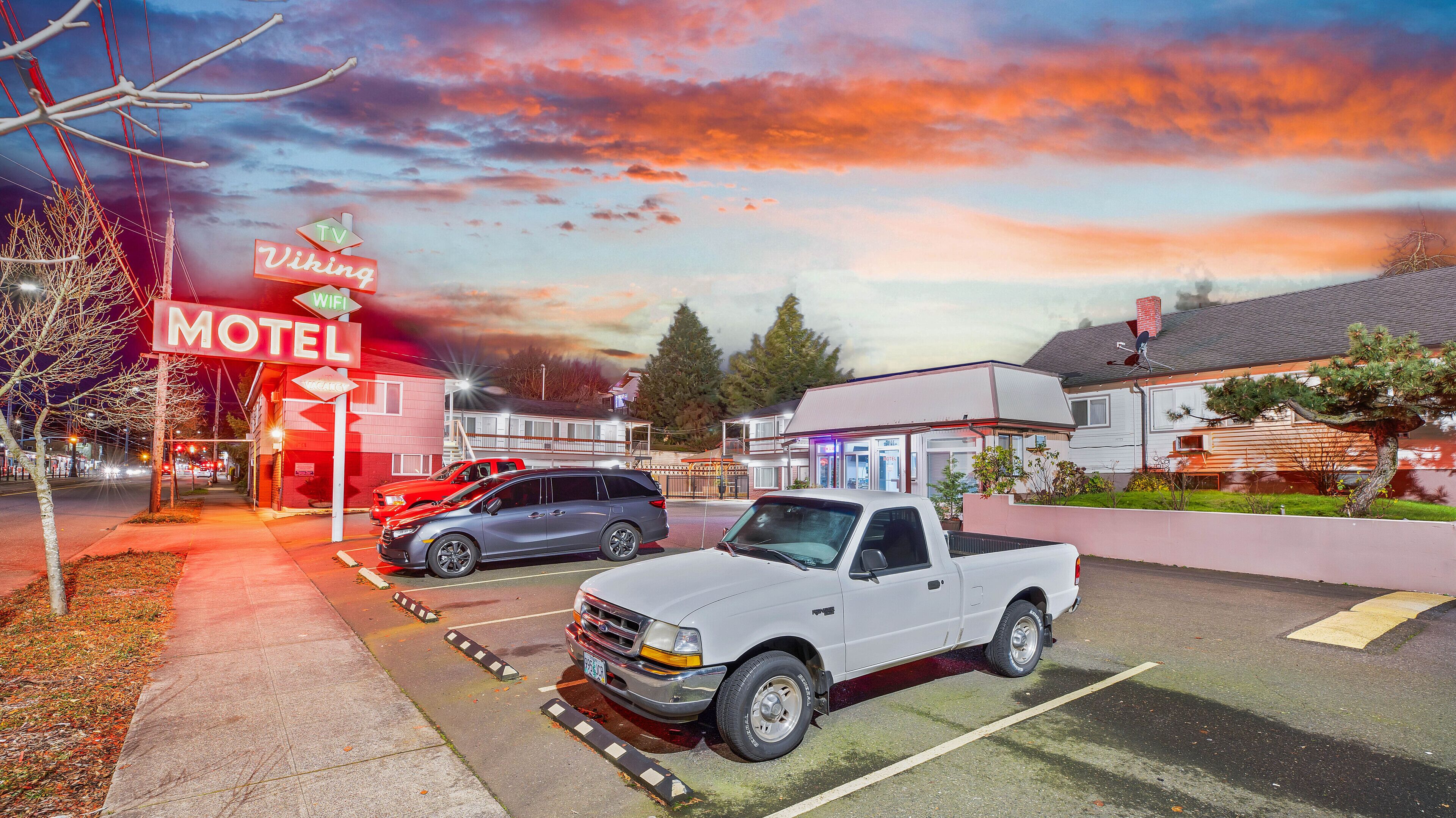 A motel with a red neon sign, a white pickup truck, and a grey SUV parked in the lot.