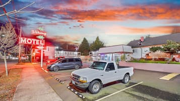 A motel with a red neon sign, a white pickup truck, and a grey SUV parked in the lot.
