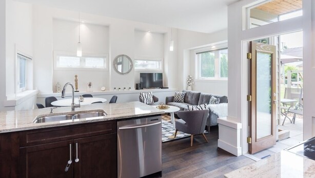 Una cocina moderna con una isla central, muebles oscuros y una zona de comedor con una mesa redonda y sofá gris.