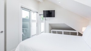 Un dormitorio con cama, televisor montado en la pared y puerta corrediza de vidrio que da a un espacio exterior.