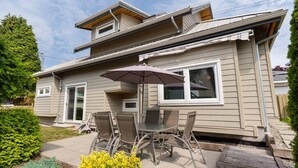 Una casa de dos pisos con un patio que cuenta con una mesa, sillas, un paraguas cubierto y una terraza de madera.