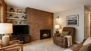A living room with a brick fireplace, a television, a sofa, and a chair. - Affordable Aspen - Heart of Downtown (Aspen)