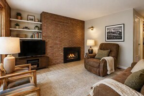 Una sala de estar con chimenea de ladrillo, televisor, sofá y sillón.