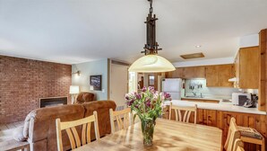 A cozy living room with a fireplace, a dining area with a wooden table and chairs, and a kitchen with wooden cabinets and a refrigerator. - Affordable Aspen - Heart of Downtown (Aspen)