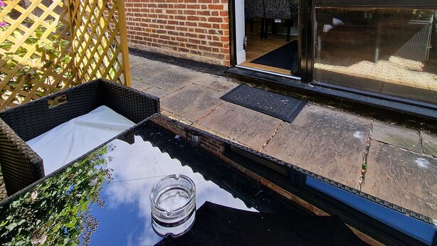 Un patio con una mesa de mimbre, un cenicero de vidrio y un muro de ladrillo.