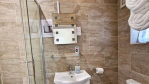 Un baño con cabina de ducha de vidrio, un lavamanos blanco con dispensador de jabón, un inodoro y una toalla colgada en la pared.