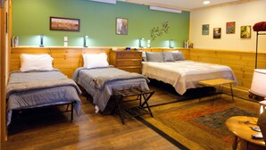 Habitación de hotel con tres camas, cabeceros de madera, una mesita con una silla y una lámpara de pie.