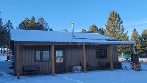 Una cabaña de madera con techo nevado, una chimenea y un porche con sillas.