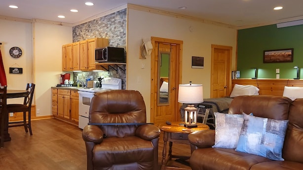 Una sala de estar acogedora con sofás de cuero, un comedor con sillas de madera y una cocina con armarios de madera y un microondas.