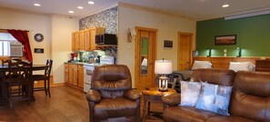 A cozy living room with leather sofas, a dining area with wooden chairs, and a kitchen with wooden cabinets and a microwave.
