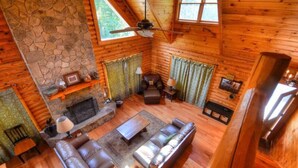 Ein gemütliches Blockhaus-Interieur mit Kamin aus Stein, Ledersofas und Deckenventilator.