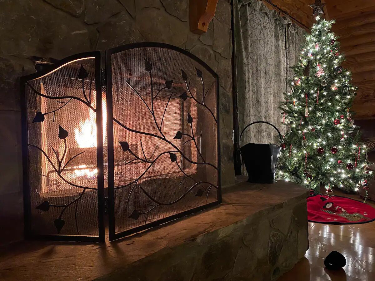 A fireplace with a decorative screen, a lit fire, and a Christmas tree with lights.