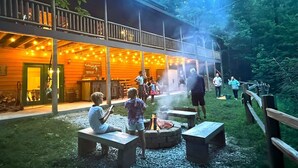 Ein rustikales Lodgehaus mit überdachter Außenbereich, einem Feuerkorb und einer Holzterrasse.