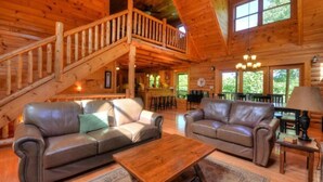 Ein geräumiges Blockhaus-Interieur mit zwei Ledersofas, einem Holztisch und einer Treppe, die in ein Obergeschoss führt.
