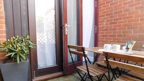 A patio area with a wooden table and chairs, a potted plant, and a brick wall. - Stay Norwich Apartments 17Colgate (Norfolk)