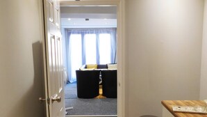 A narrow hallway leading to a room with a bed, a small table, and a window with curtains. - Stay Norwich Apartments 17Colgate (Norfolk)