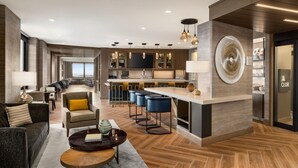 A modern hotel lobby with a bar area, seating, and a large screen. - Marriott New York JFK Airport (Jamaica)