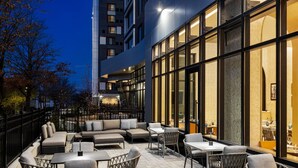 An outdoor seating area with sofas, chairs, and tables, surrounded by a black metal fence. - Marriott New York JFK Airport (Jamaica)