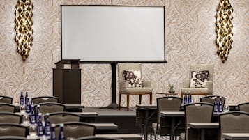 A conference room with a large screen, two chairs with decorative pillows, and tables with water bottles.