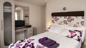 A bedroom with a bed, a TV on a dresser, a mirror, and a nightstand with a lamp.