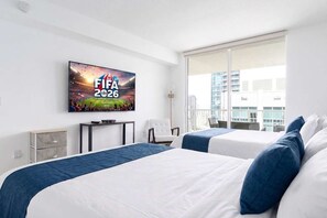 Habitación de hotel con dos camas, un televisor mostrando FIFA 2026, un escritorio y una silla.