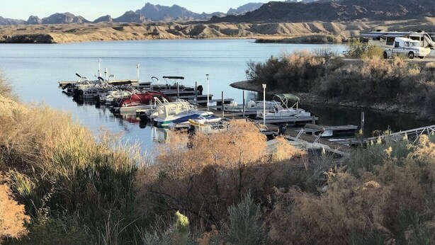 A marina with boats docked, surrounded by dry grass and hills in the background.