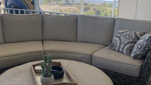 A corner sofa with a round ottoman, a tray with a cactus, and a view of the landscape.