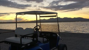 A golf cart on a sandy beach with a sunset in the background.
