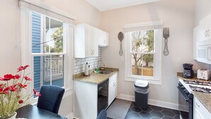 Una cocina compacta con armarios blancos, encimera de granito, estufa a gas y ventana con vistas al exterior.