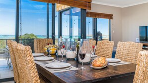 Un coin repas avec vue sur l’océan, des chaises en osier, une table en bois et un téléviseur.