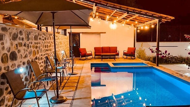 Un área de piscina con muro de piedra, asientos e iluminación con guirnaldas.