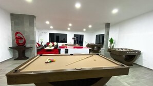 Una mesa de billar en una sala moderna con un sofá y un recipiente decorativo grande.