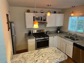 A kitchen with white cabinets, a stainless steel stove, a microwave, and a sink. There are overhead lights and a window with blinds. - Trinidad Harbor Ocean Views l 2 Bedrooms 2 Bathrooms (Trinidad)