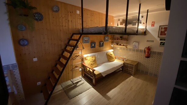 Une pièce chaleureuse avec un mur en bois, un canapé, une échelle et un luminaire suspendu.