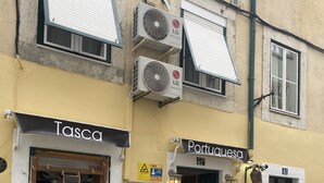 Un immeuble abritant deux boutiques, nommées « Tasca » et « Portuguesa ». Il y a des tables et des chaises à l’extérieur, et l’immeuble est équipé de climatiseurs sur sa façade.