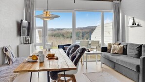 Un salon moderne avec une table à manger en bois, un canapé gris et une grande fenêtre donnant sur l’extérieur.