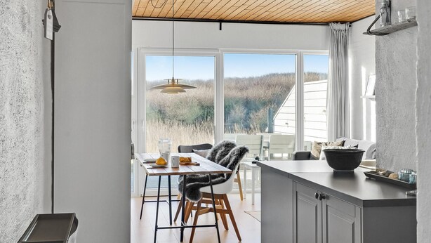 Une cuisine moderne avec un plafond en bois, de grandes fenêtres et un coin repas offrant une vue sur l’extérieur.
