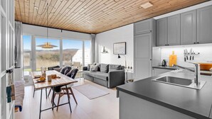 Une cuisine moderne avec des meubles gris, un plafond en bois et une grande fenêtre donnant sur un paysage naturel.