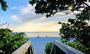A beach view with a wooden walkway leading to the shore, surrounded by greenery. - Steps to Vanderbilt Beach! (Naples)