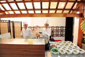 Ristorante con cuochi che preparano cibo, un tavolo del buffet con diversi piatti e un soffitto in legno tradizionale.