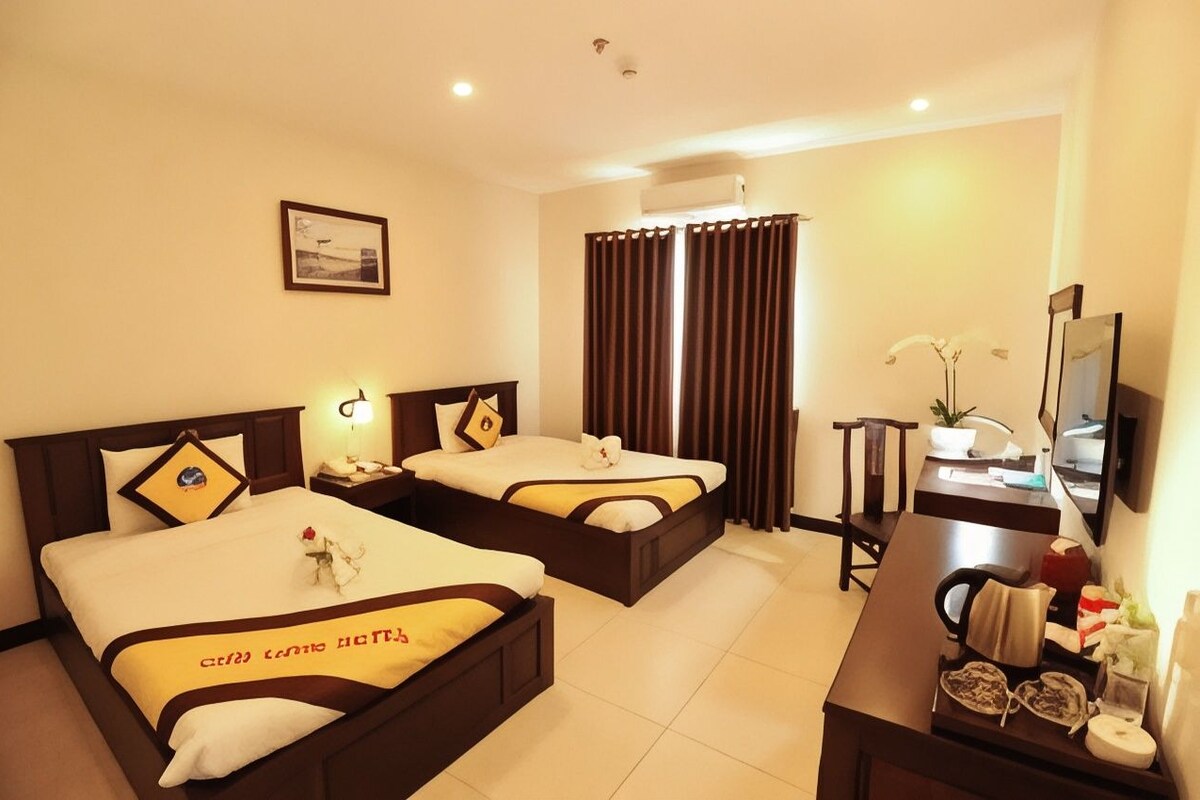 A hotel room with two beds, a desk, a chair, a TV, and a window with curtains.
