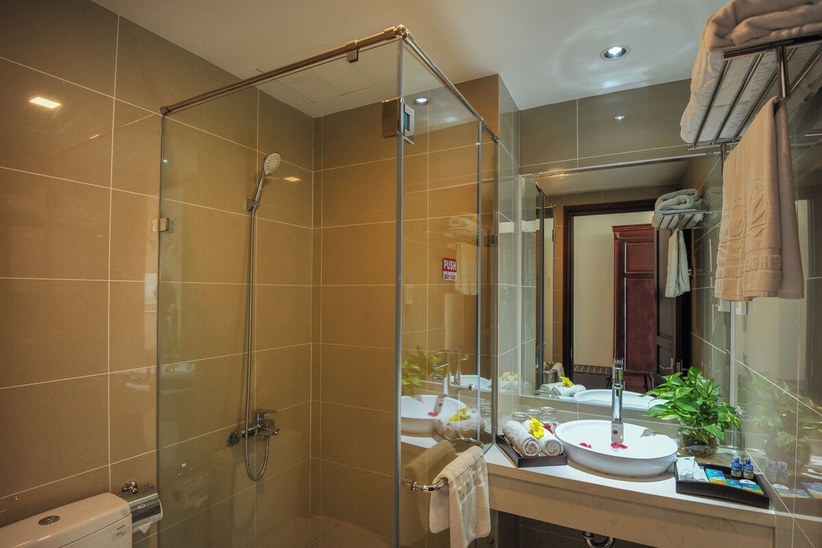 A modern bathroom with a glass-enclosed shower, a sink with toiletries, and a mirror reflecting the room.