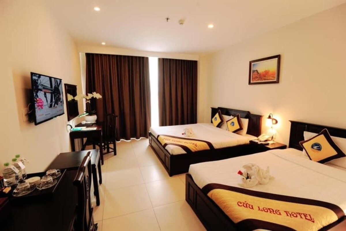 A hotel room with two beds, a desk, a television, and a painting on the wall.