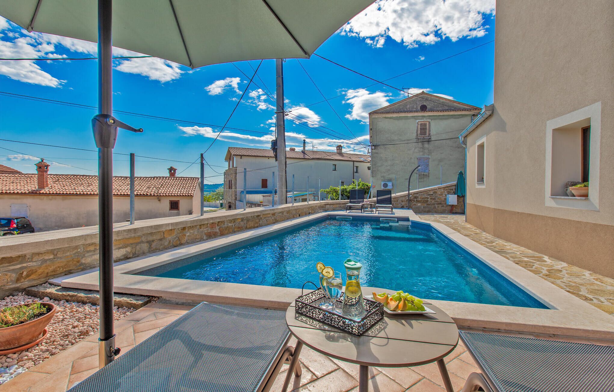 A swimming pool with a table and chairs, surrounded by buildings and a clear sky.
